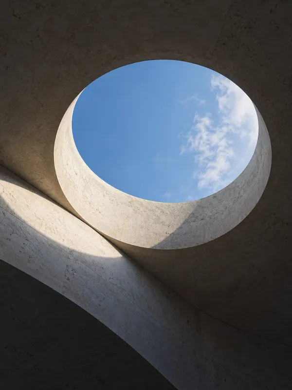 Blue sky through a circular skylight in a sculptural stone ceiling